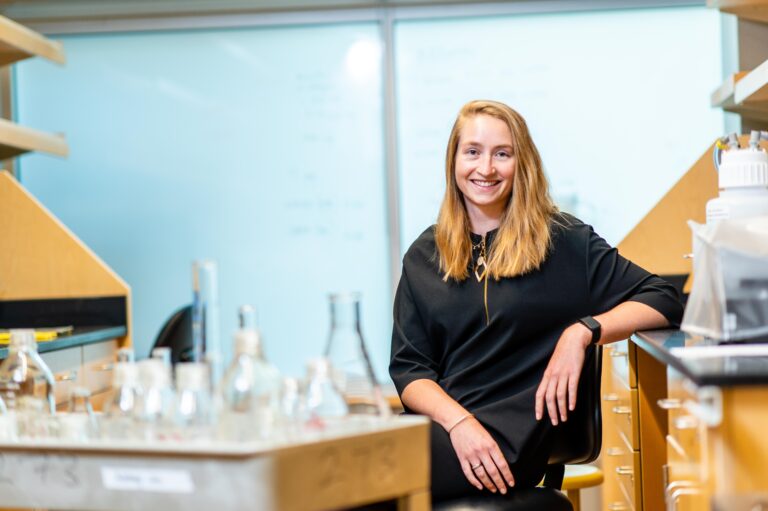 a woman in black shirt sits with glass flasks in a science laboratory