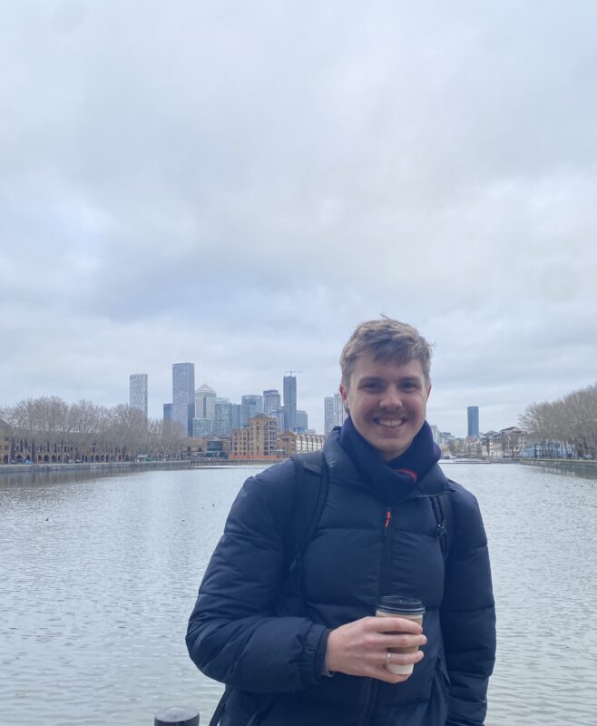 Thomas Worthington, pictured smiling and holding a cup of coffee in front of a city backdrop.