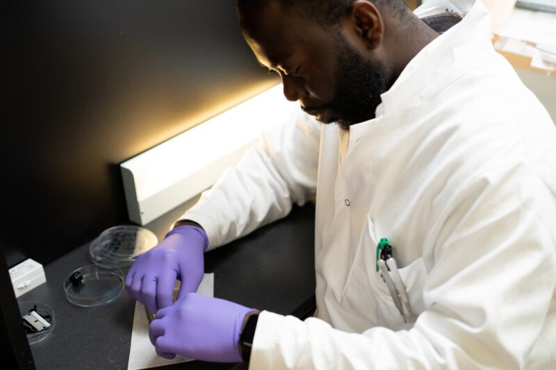 Eric Boateng sits at a lab bench, looking down at his hands to prepare a microscope slide.
