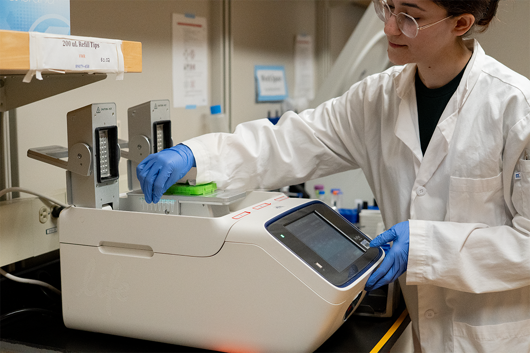 Erdoğan reaches across a PCR machine in the lab. 